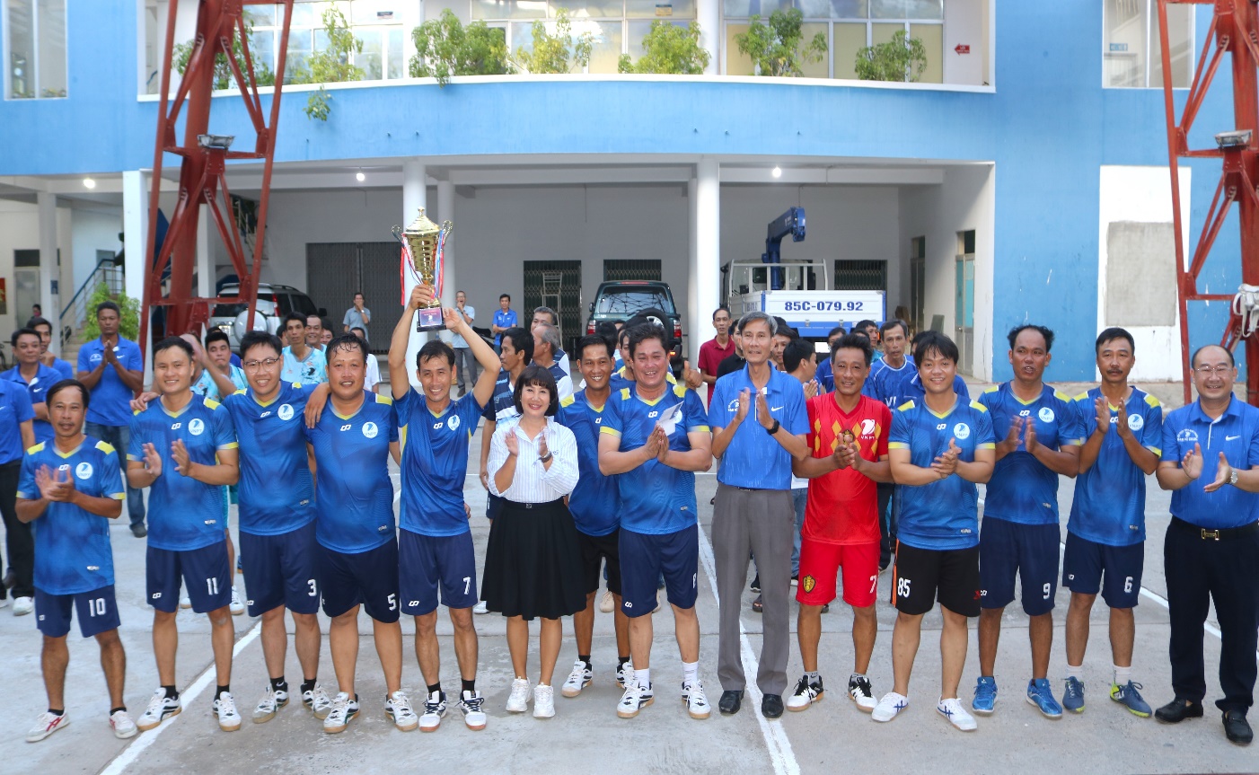 A group of people in blue shirts holding up a trophy
Description automatically generated
