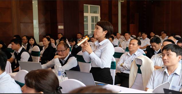 A person speaking into a microphone in front of a group of people
Description automatically generated