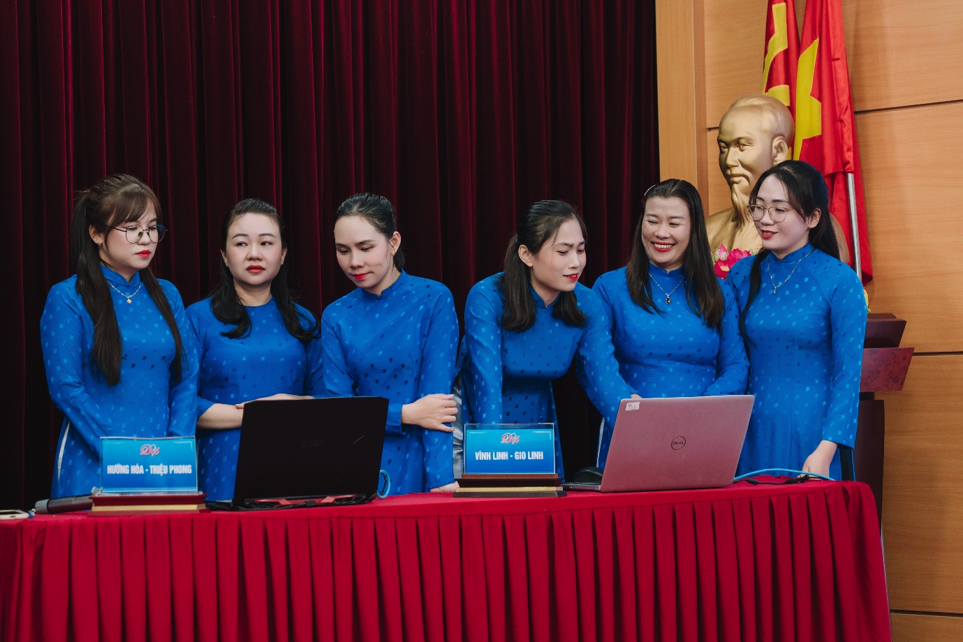 A group of women in blue dresses standing in front of a table with laptops
Description automatically generated