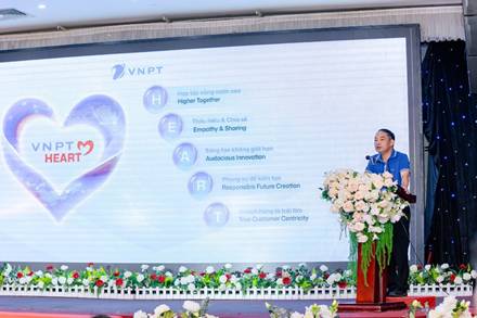 A person standing on a podium with flowers and a large screen

Description automatically generated