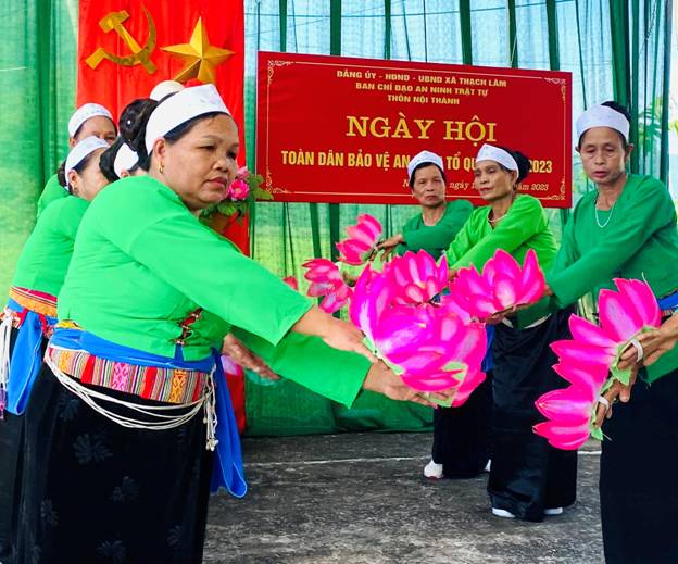 A group of women in green shirts and white headdresses holding pink flowers

Description automatically generated