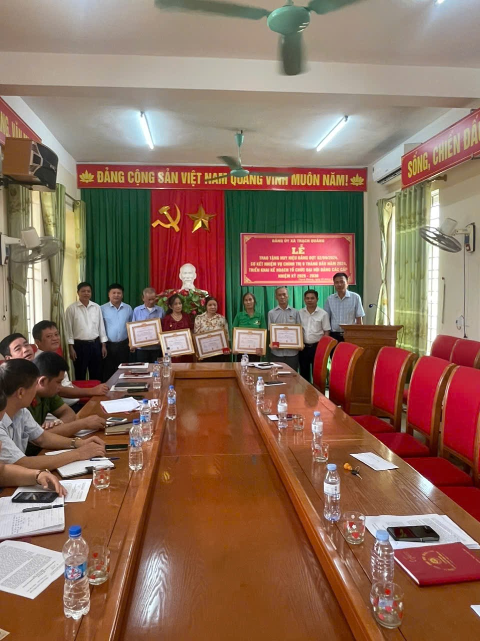 A group of people standing around a long table with red chairs
Description automatically generated