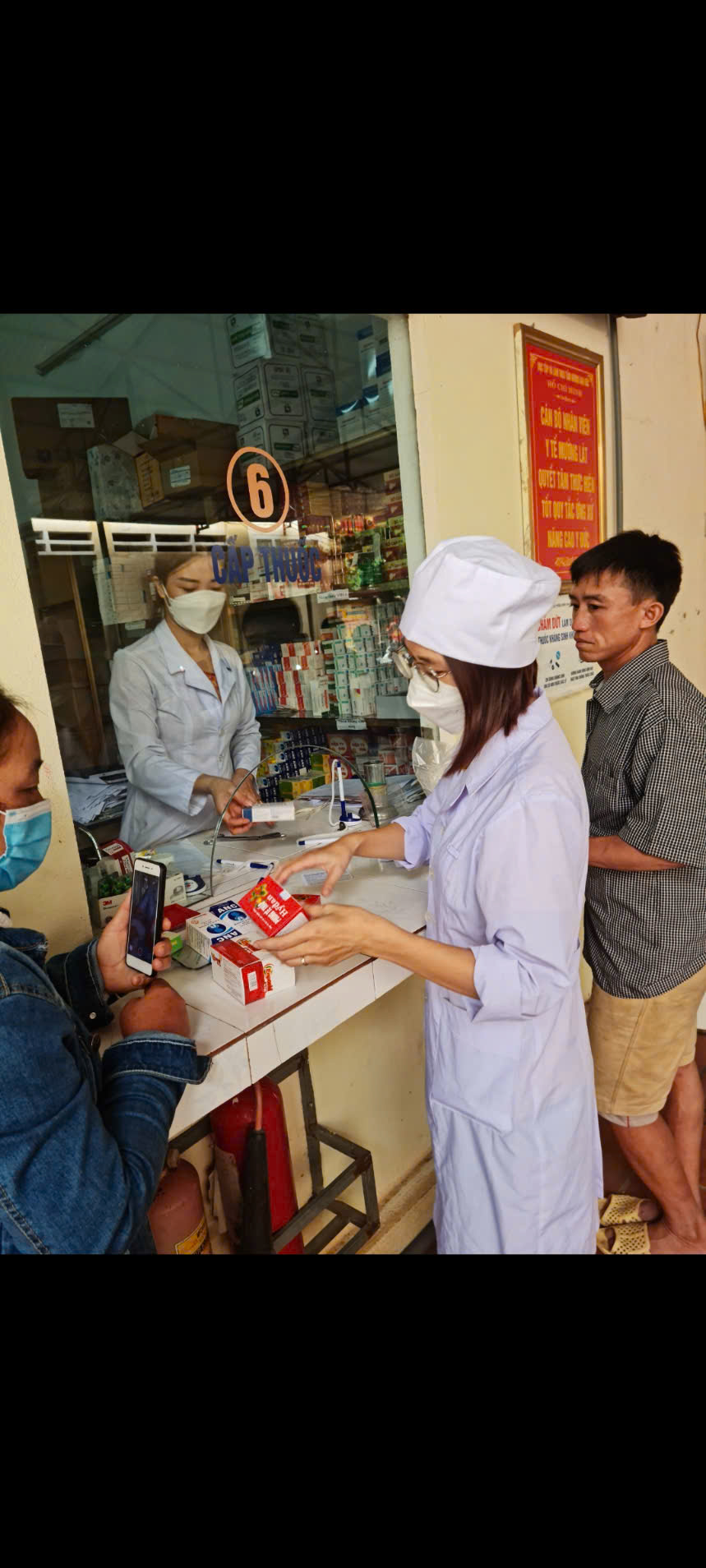 A person wearing a white coat and mask standing in front of a counter with other people in the background
AI-generated content may be incorrect.