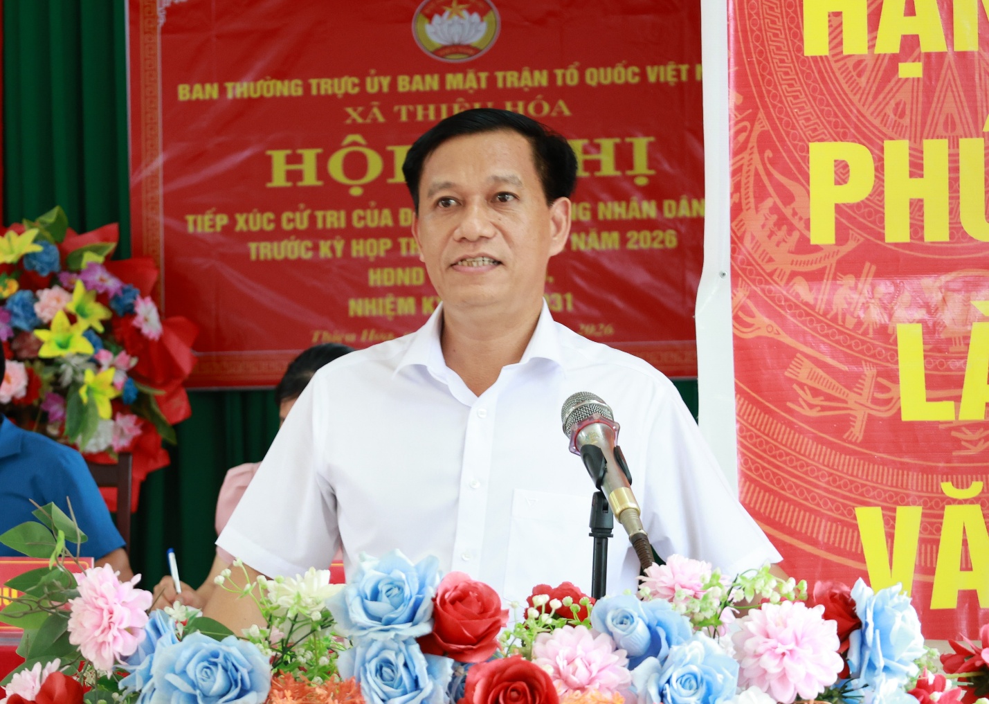 A person standing at a podium with microphones and flowers
Description automatically generated
