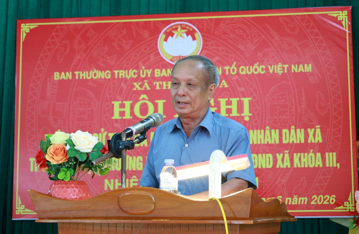 A person standing at a podium with a microphone and flowers
Description automatically generated