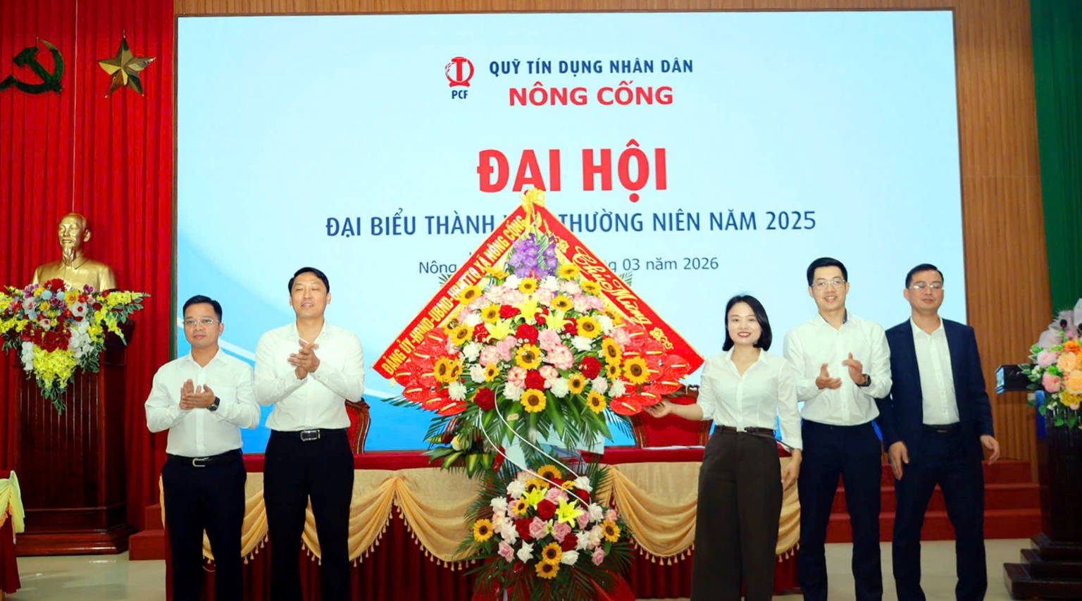 A group of people standing in front of a large screen
Description automatically generated