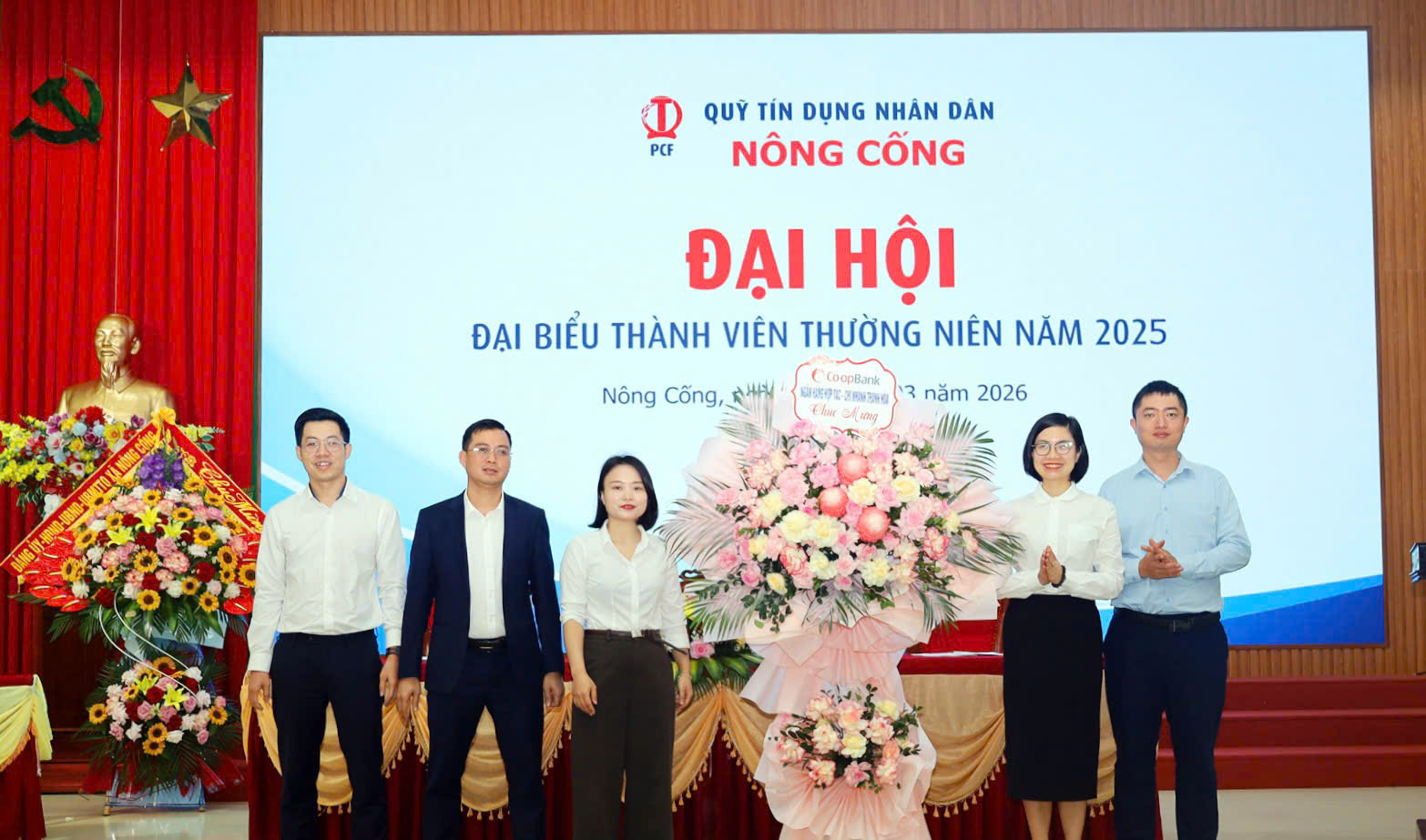 A group of people standing in front of a large screen
Description automatically generated