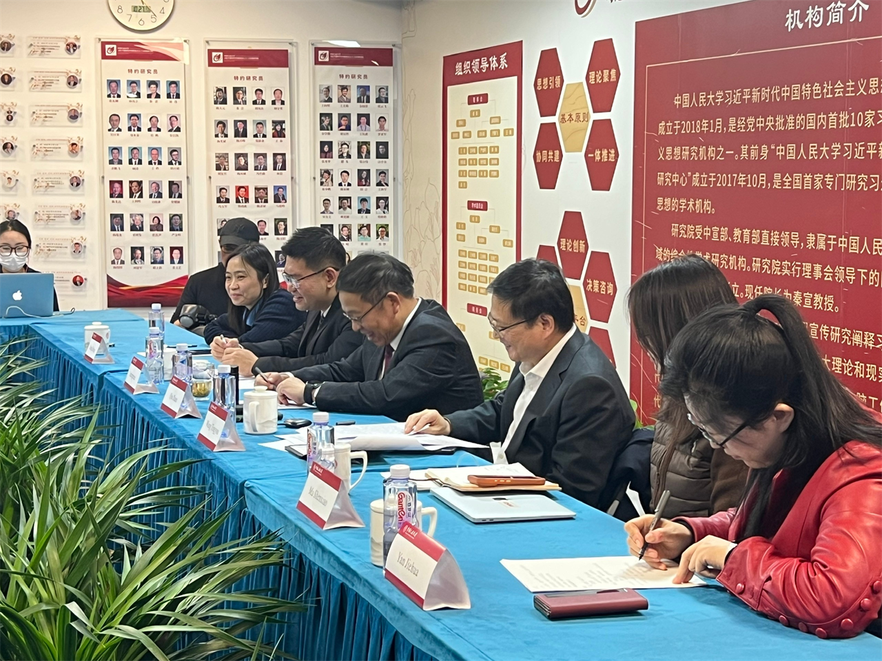 Description: The image shows a group of people seated at a table, all engaged in signing documents or working on paperwork. The background features a red banner with Chinese text, likely related to an academic or research institution.
AI-generated content may be incorrect.