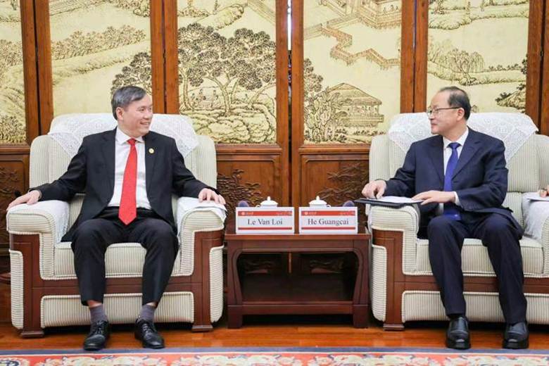 The image depicts two individuals, Le Van Loi and He Guangcai, seated in a formal setting with traditional decorations and a table displaying their names.
AI-generated content may be incorrect.