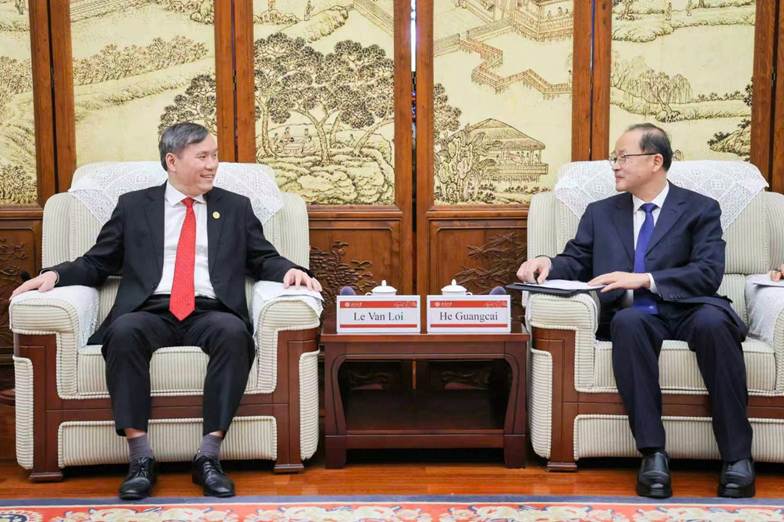 The image depicts two individuals, Le Van Loi and He Guangcai, seated in a formal setting with traditional decorations and a table displaying their names.
AI-generated content may be incorrect.