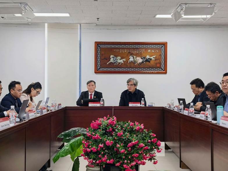 The image depicts a conference room with a large round table surrounded by people, decorated with a vase of flowers, and a wall decoration featuring a Chinese character.
AI-generated content may be incorrect.